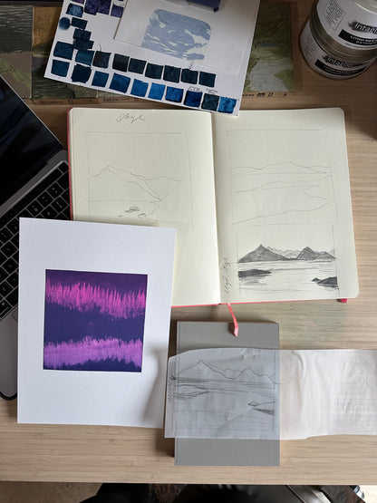 Artistic work on a desk with sketches, prints, and a laptop.